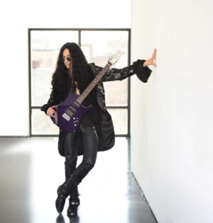 Mike Campese - holding guitar leaning against wall with hand in empty room